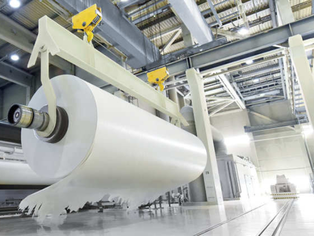 large roll of paper on a crane in a mill for the production of paper for further processing in a printing plant - recycling of waste paper